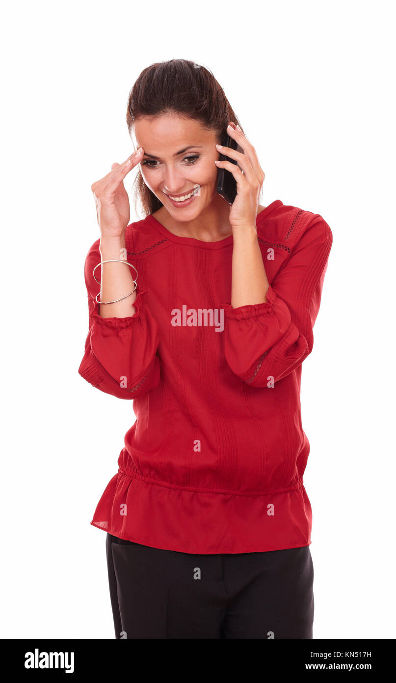 Portrait of happy latin lady on red shirt talking on her phone while standing and smiling on isolated studio. Stock Photo