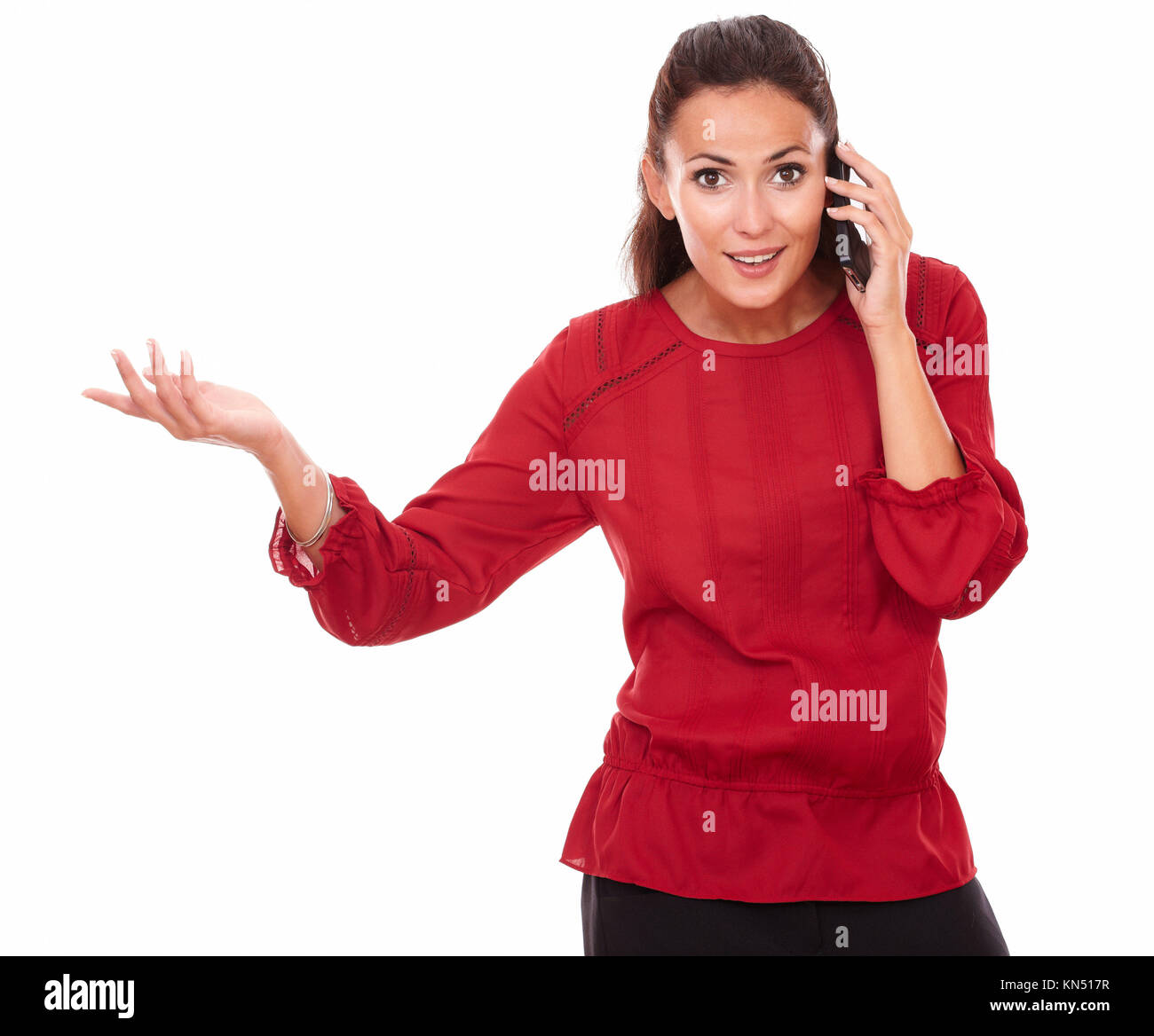 Portrait of friendly young lady on red blouse talking on her phone while looking at you and standing on isolated white background - copyspace. Stock Photo
