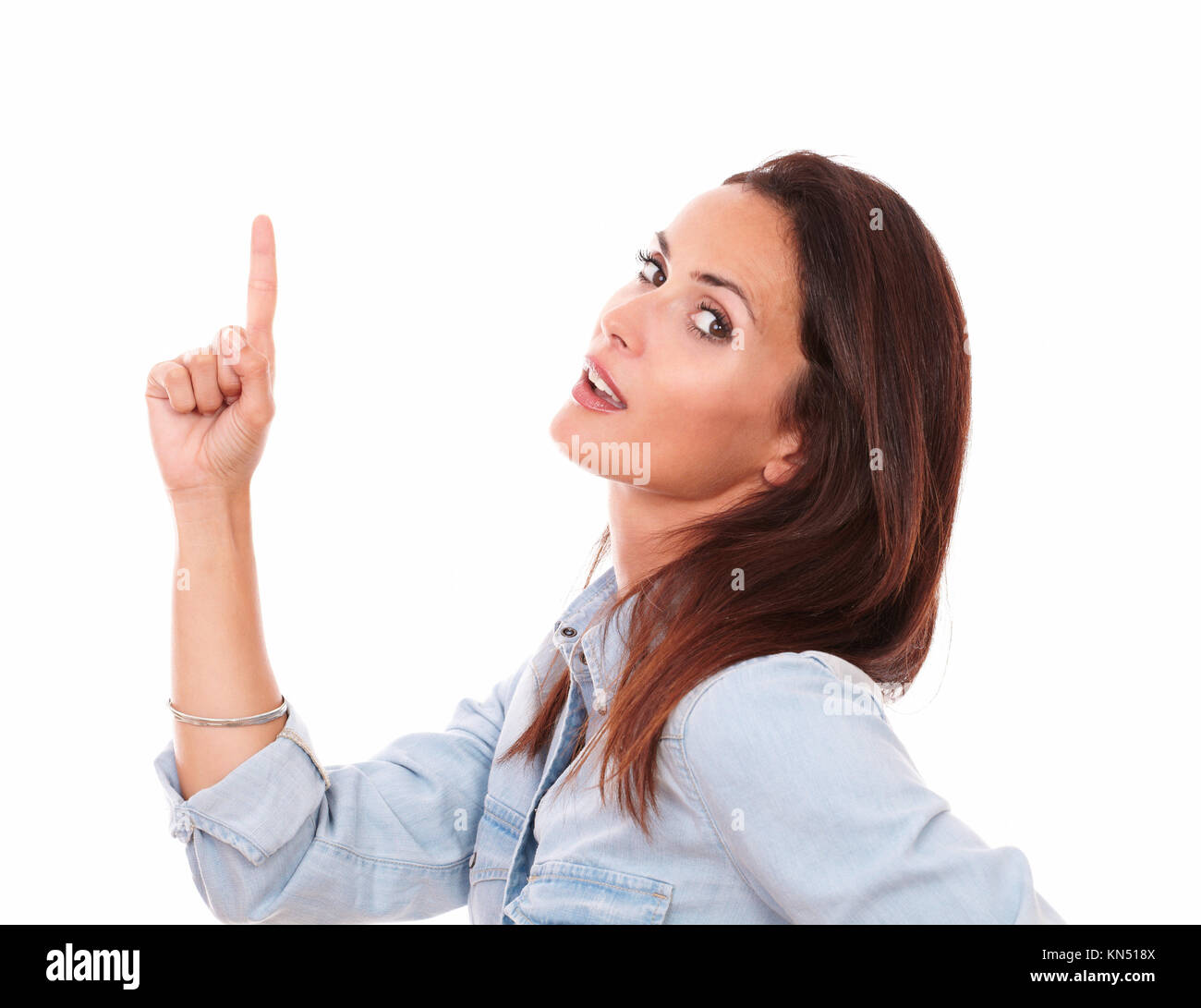 Portrait of attractive female on blue shirt pointing up and looking at you on isolated white background - copyspace. Stock Photo