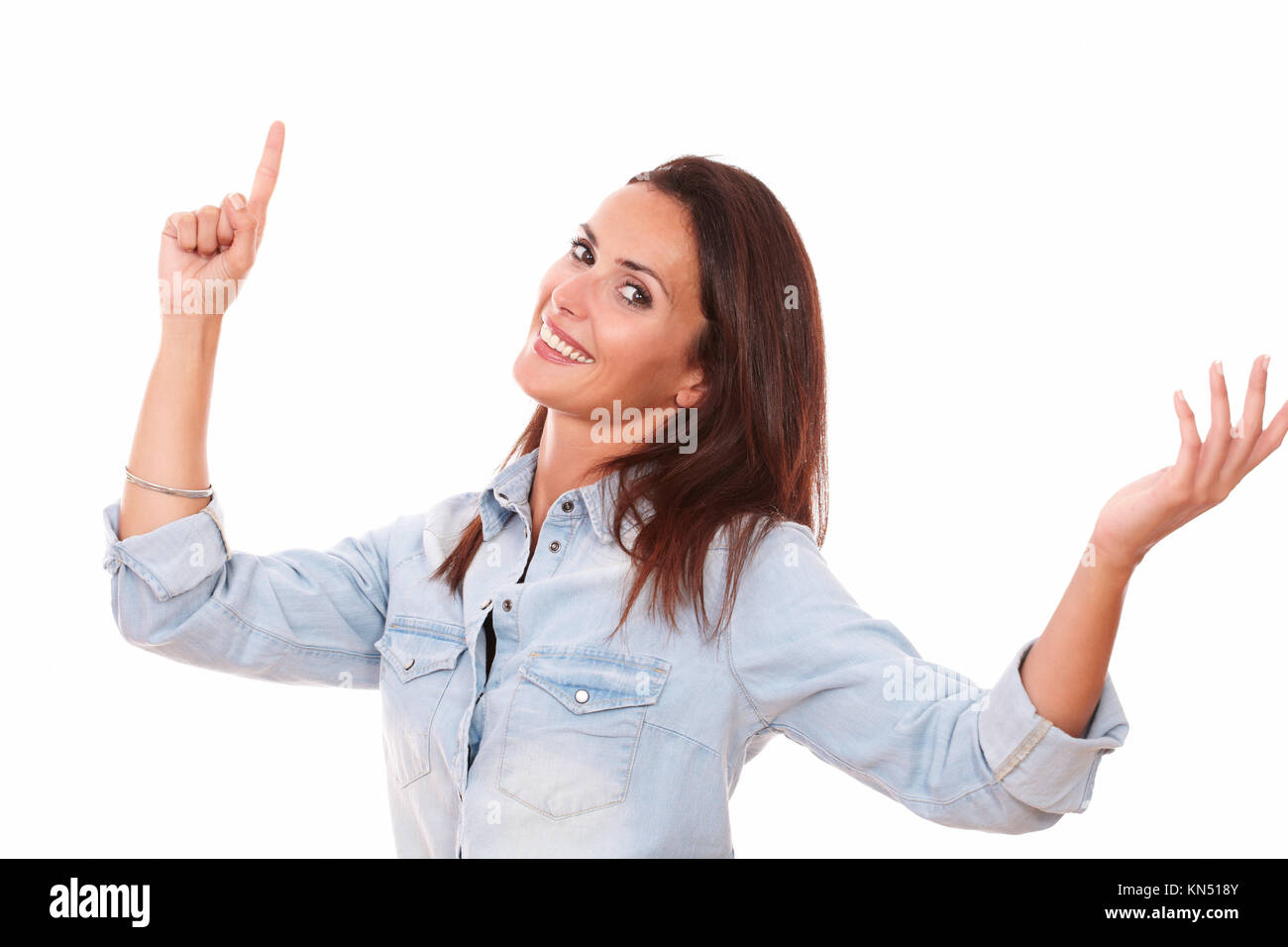 Portrait of friendly young lady on blue blouse pointing up and smiling at you on isolated white background - copyspace. Stock Photo