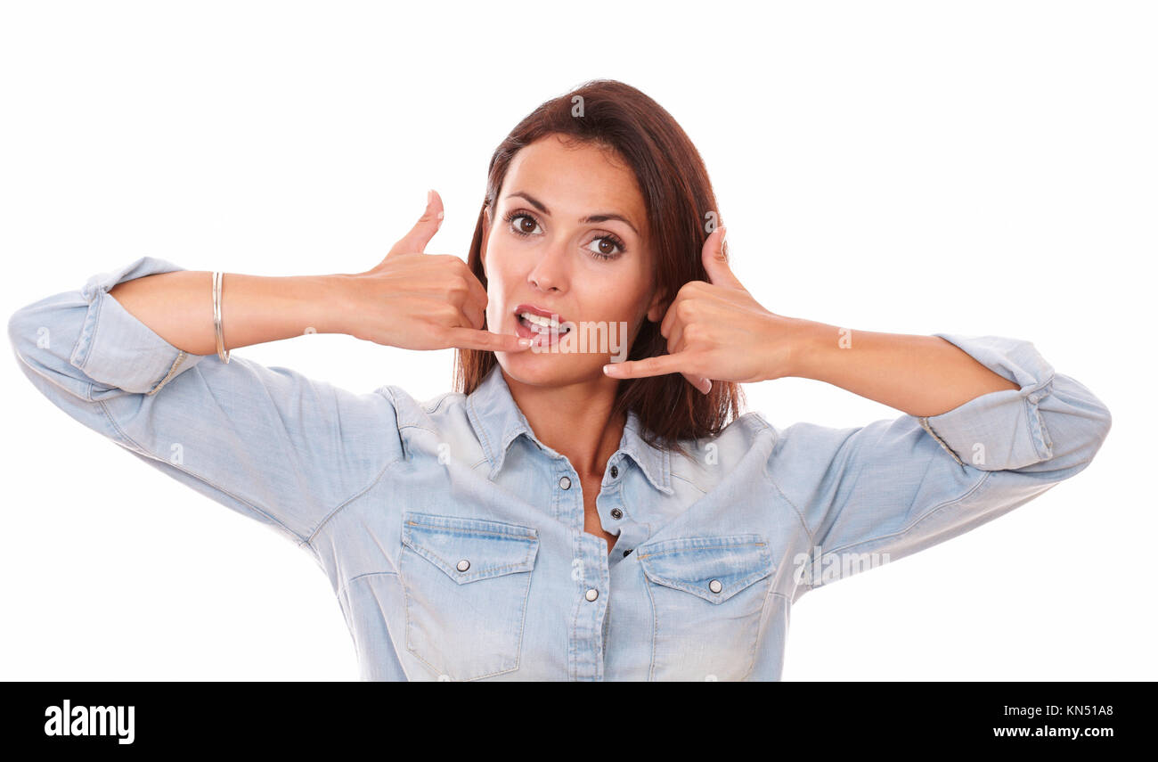 Portrait of friendly adult brunette on blue shirt with phone gesture smiling at you with funny face on isolated studio. Stock Photo