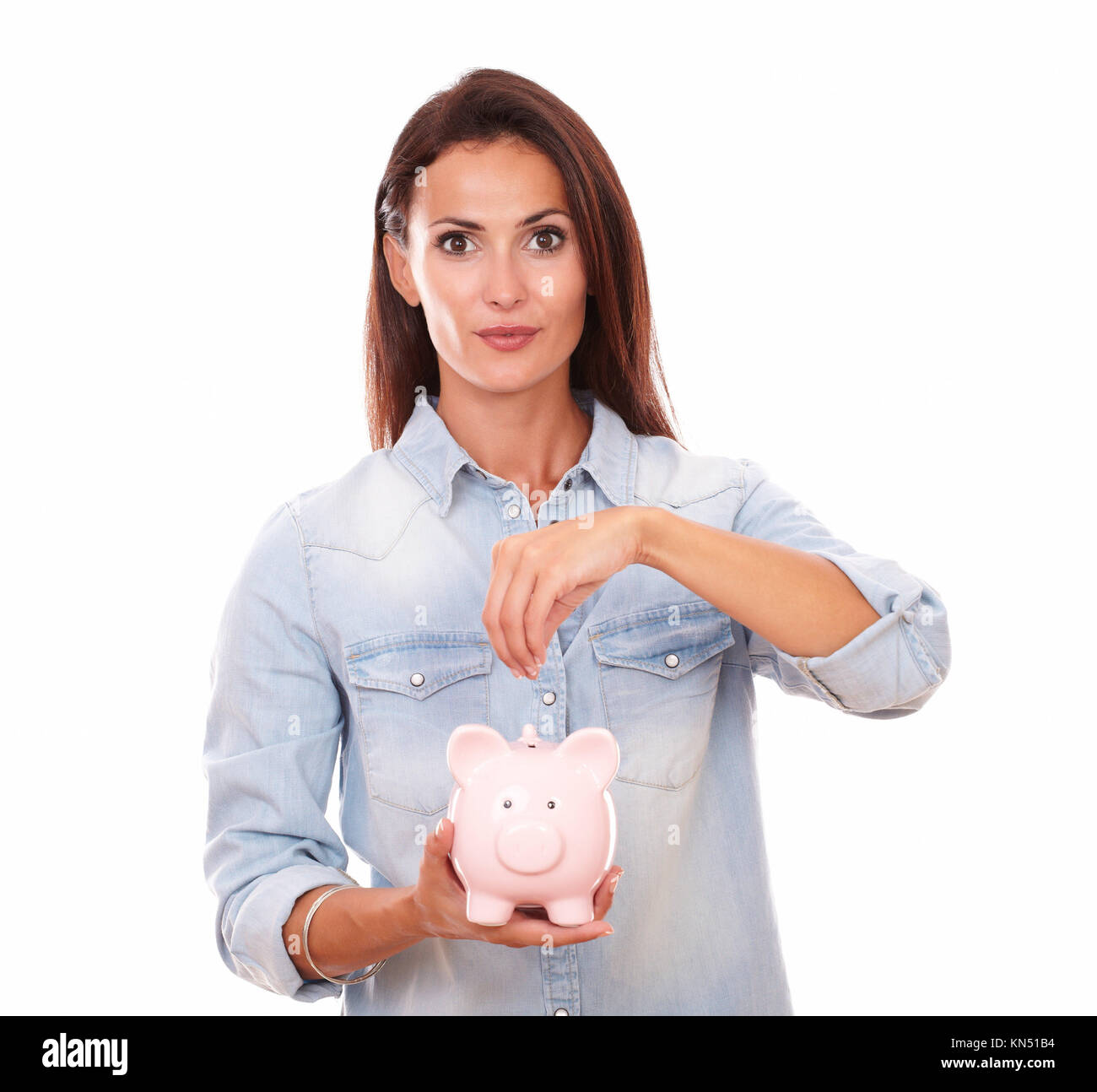 Portrait of lovely latin lady savings money in a piggybank while standing and looking at you on isolated studio. Stock Photo
