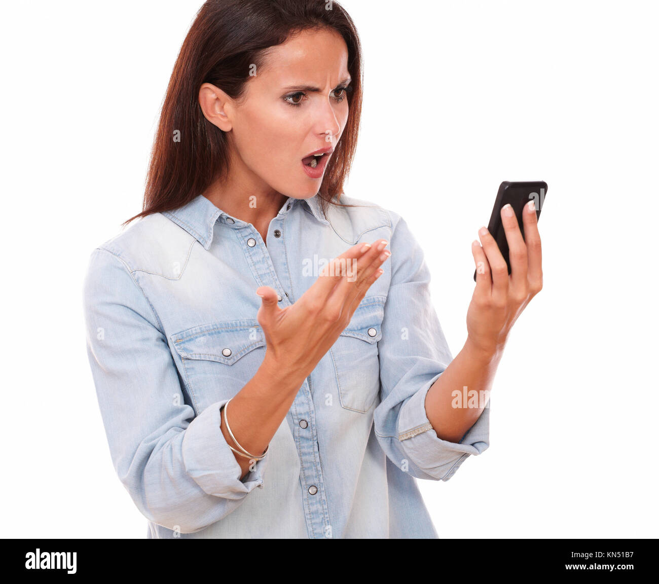 Portrait of angry adult female on blue blouse reading a message on her cell while screaming on isolated white bacckground. Stock Photo