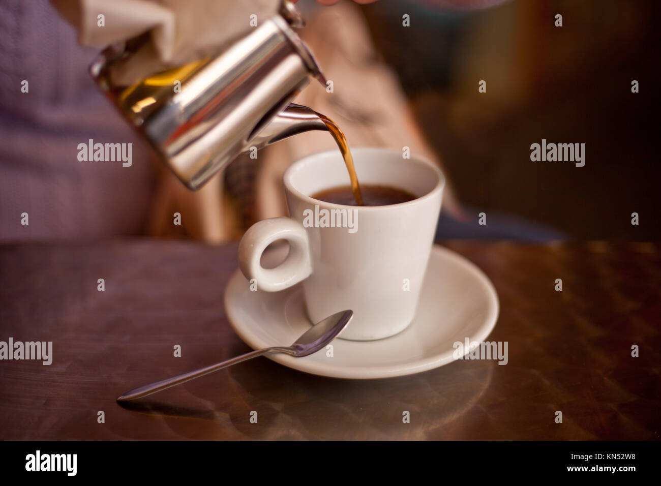 Serving tea from a metal teapont in a white ceramic cup on restaurant terrace table. Selective focus. Stock Photo