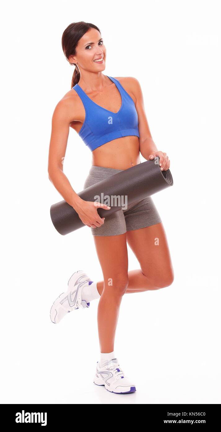 Slim female brunette in training clothes holding exercise mat against white background. Stock Photo