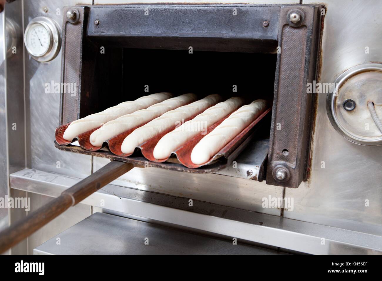 Baker putting bread dough into the oven. Selective focus. Manufacturing process of spanish bread. Stock Photo