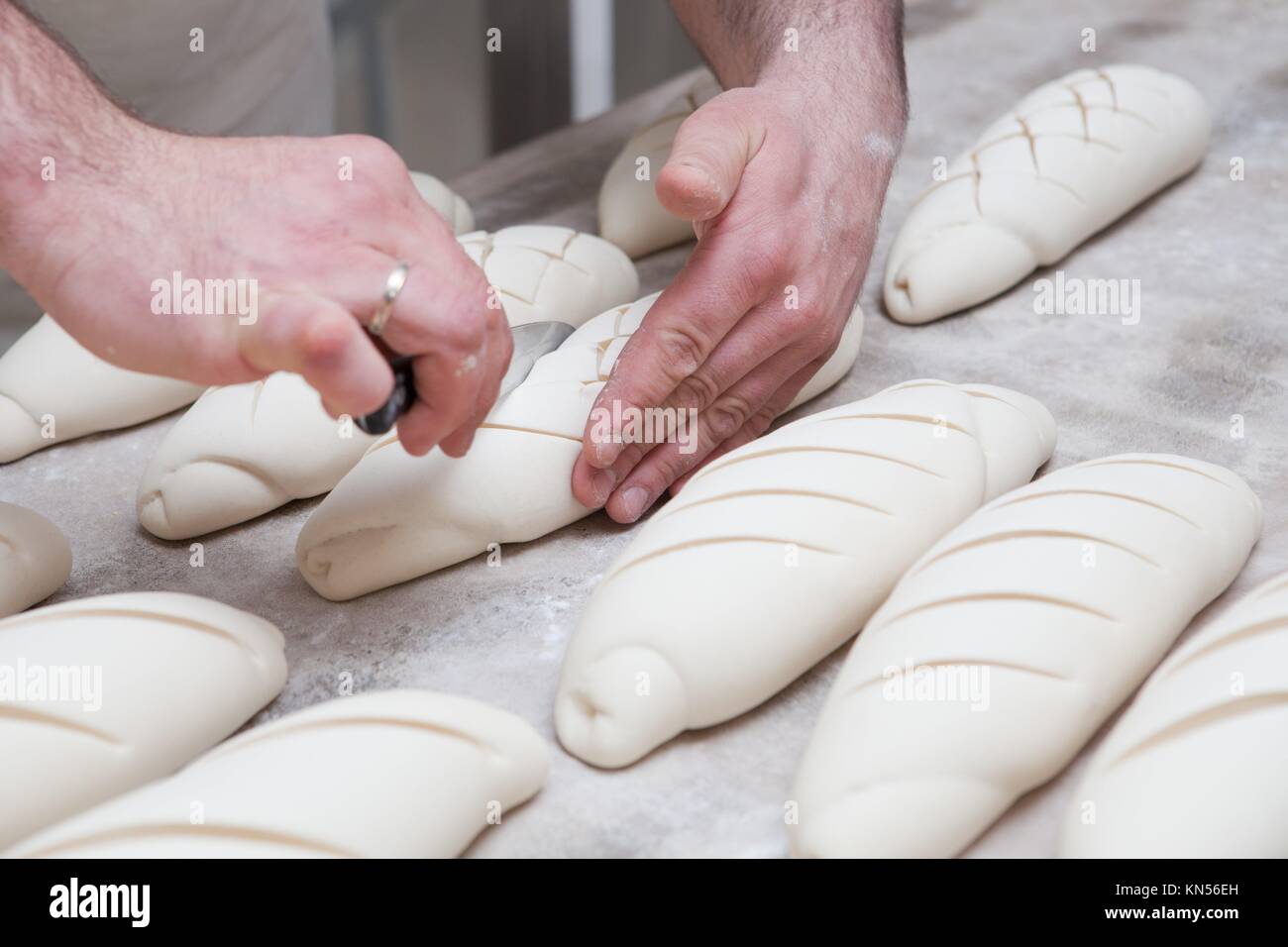 Baker making patterns on raw bread using a knife to shape the dough prior to baking. Manufacturing process of spanish bread. Stock Photo