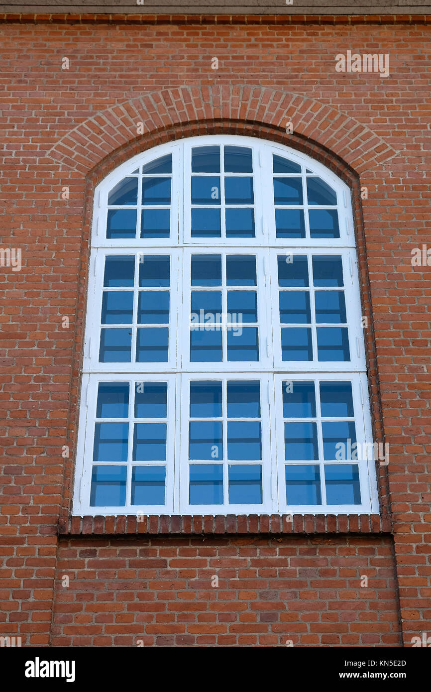 Big tall old white painted wood window with an arched top in a red brick facade Stock Photo