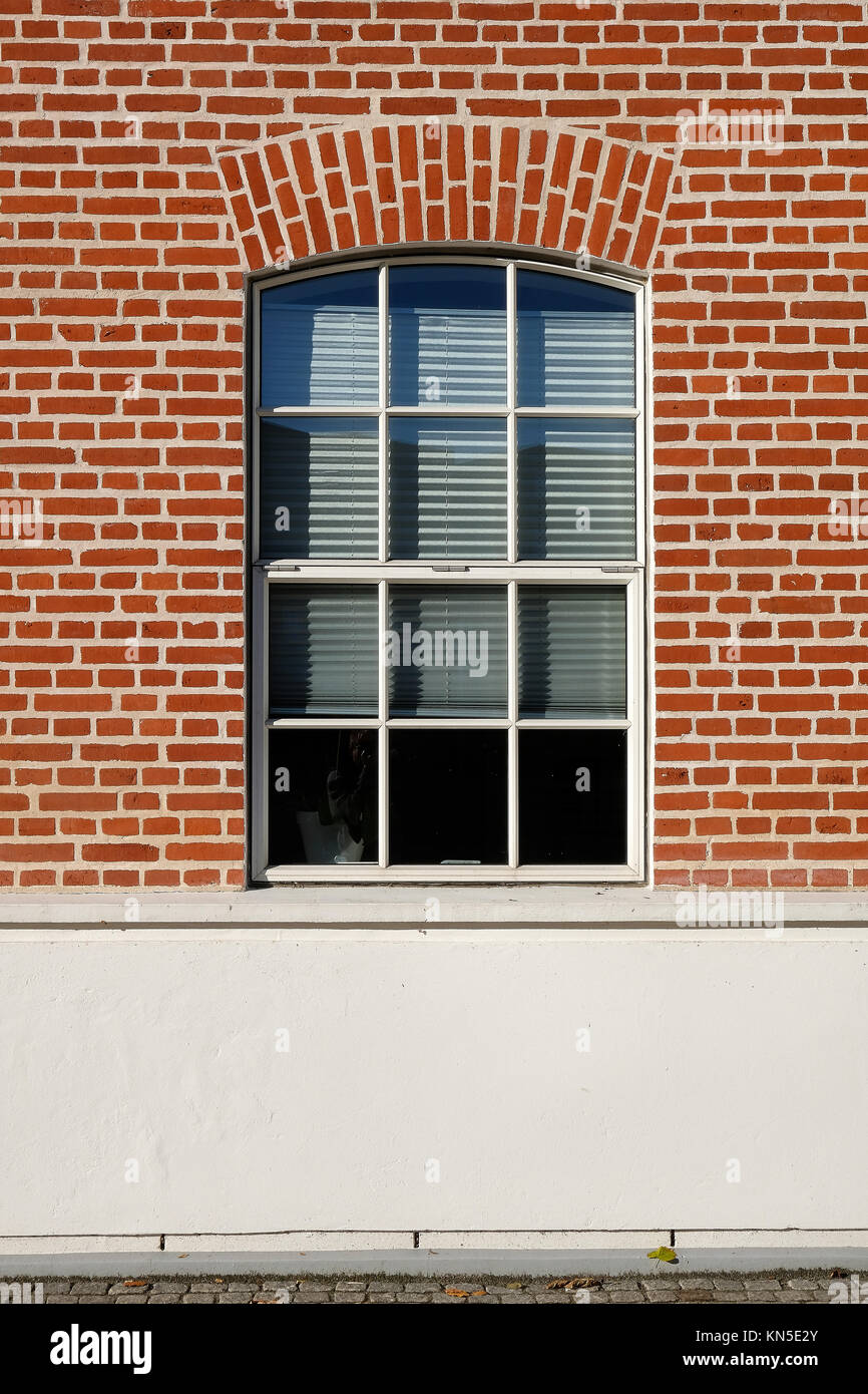 Tall arch format metal barn style window with small glazing pattern, in a red brick facade Stock Photo