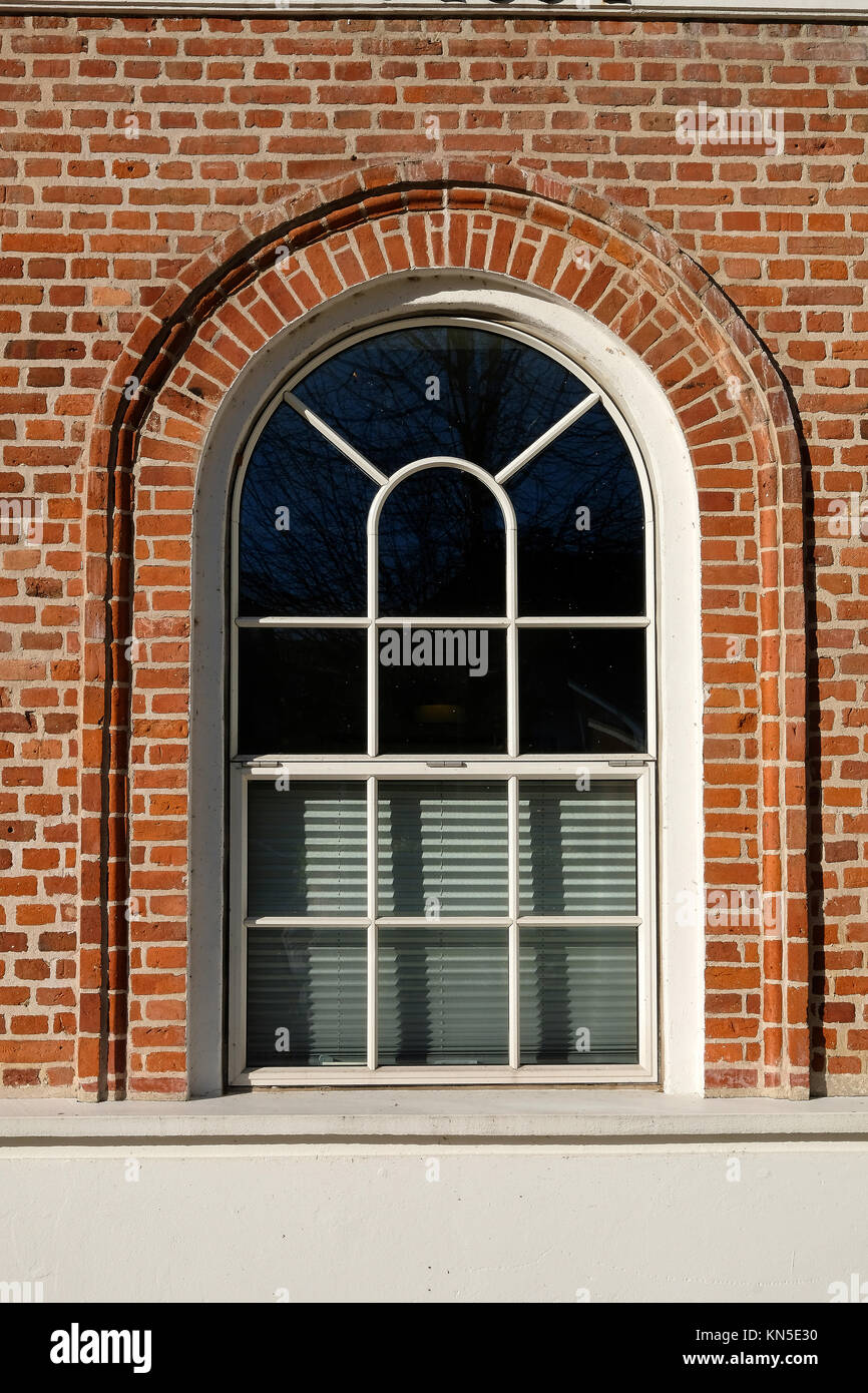 Tall rounded format metal barn style window with designed glazing pattern, in a red brick facade Stock Photo