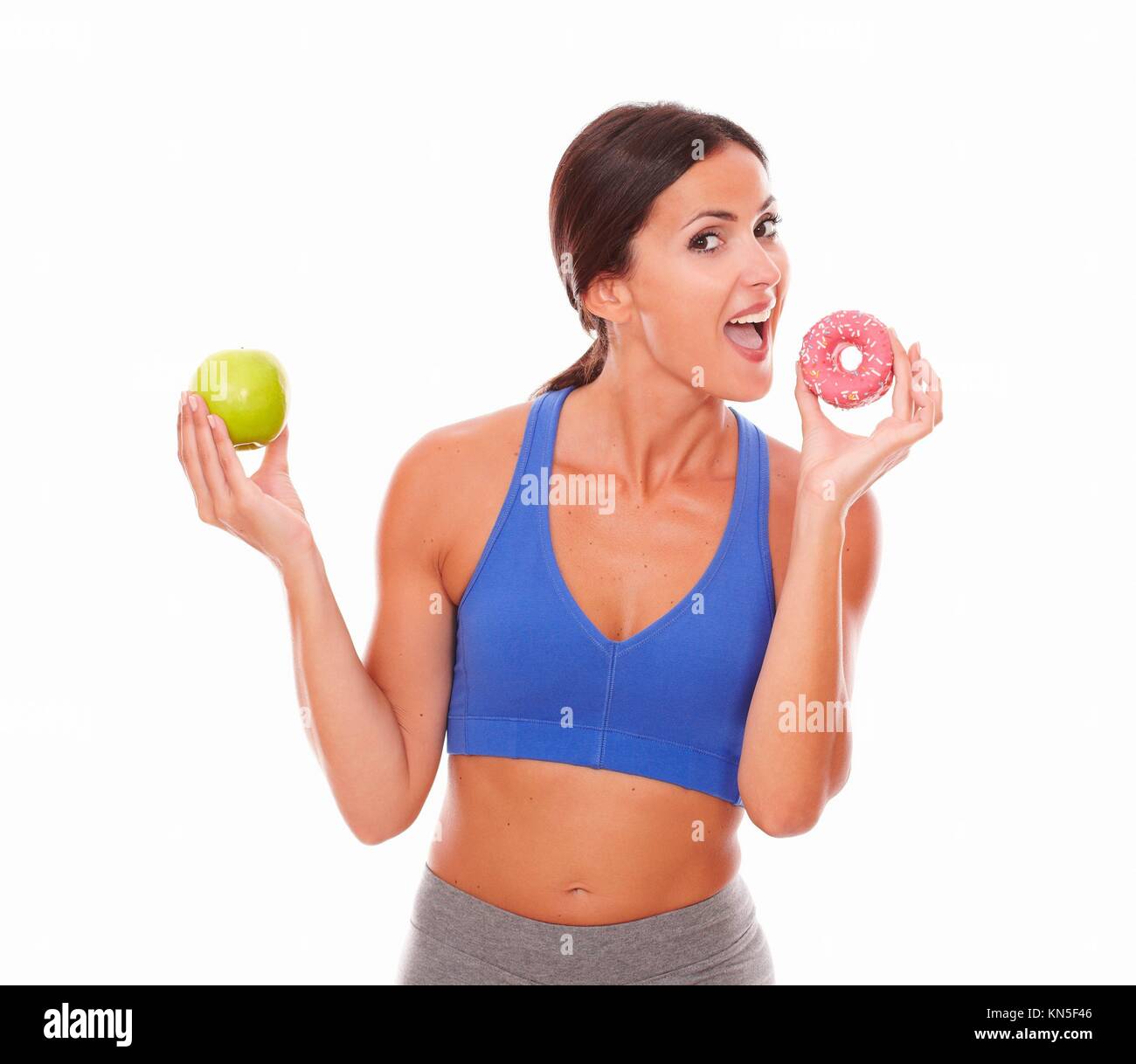 Lady wearing sports outfit biting sugary cake against white background. Stock Photo