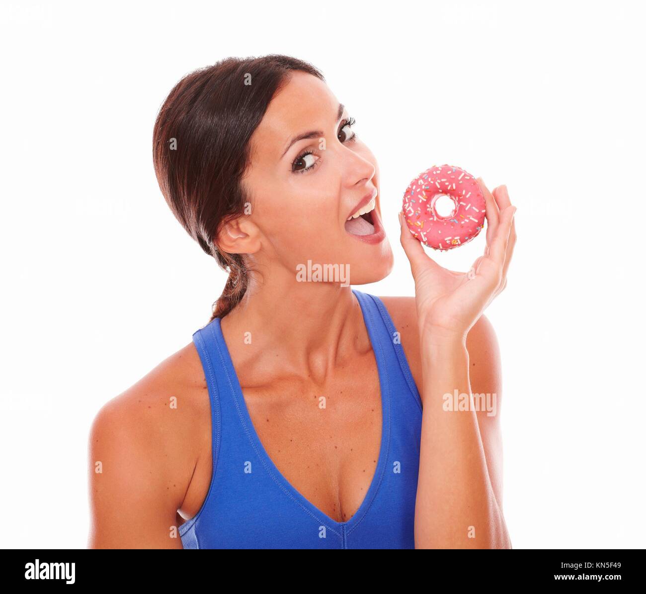 Brunette female taking a bite on sugary cake looking at you on isolated background. Stock Photo