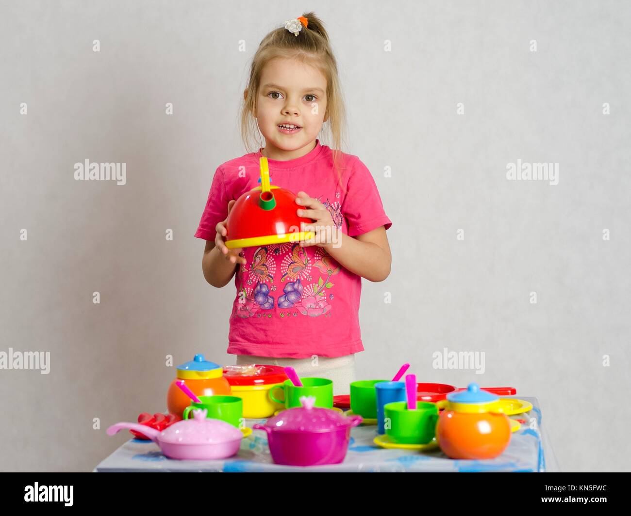 Girl plays child kitchen utensils. She picked up the teapot and looks