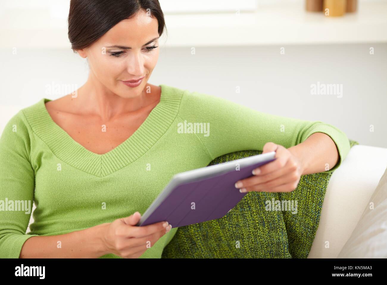 Waist up portrait of a caucasian woman in a green tank top using a tablet indoors. Stock Photo