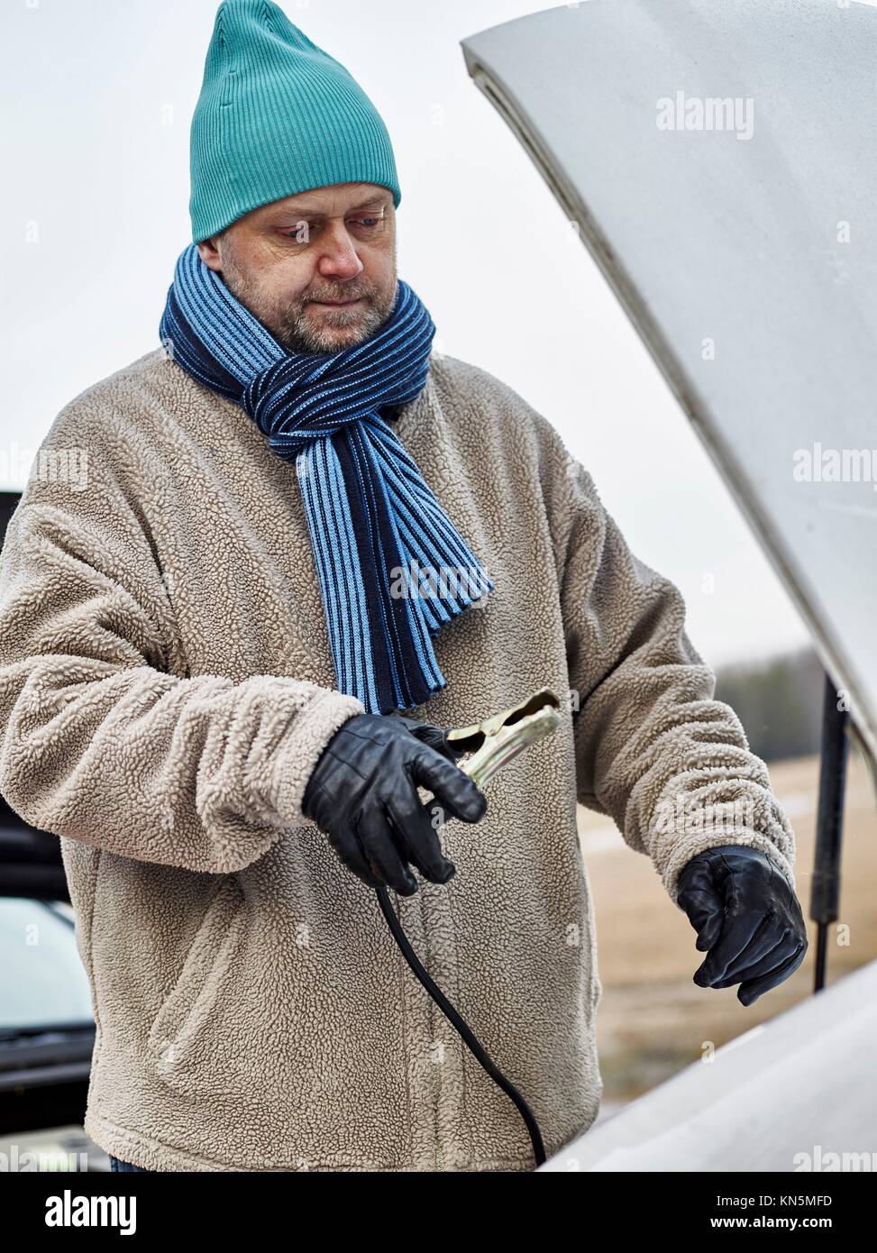 Mid adult man use a jumper cables between the two vehicles. Stock Photo