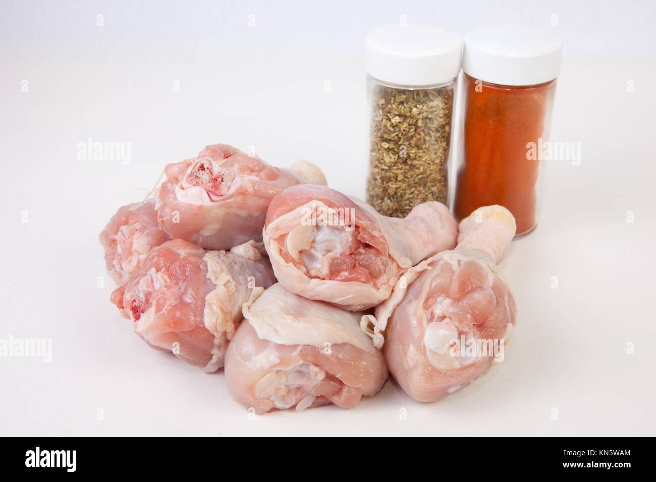Chicken thighs or legs with spice bottles. Isolated over white background. Stock Photo