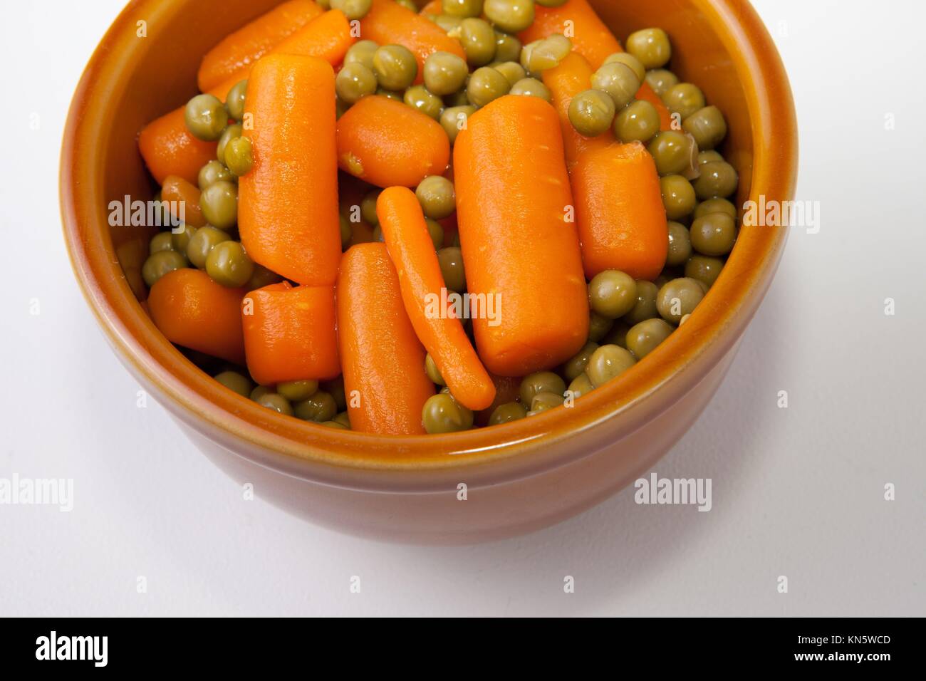 Boiled carrots and green peas on rustic glazed clay bowl. Isolated over