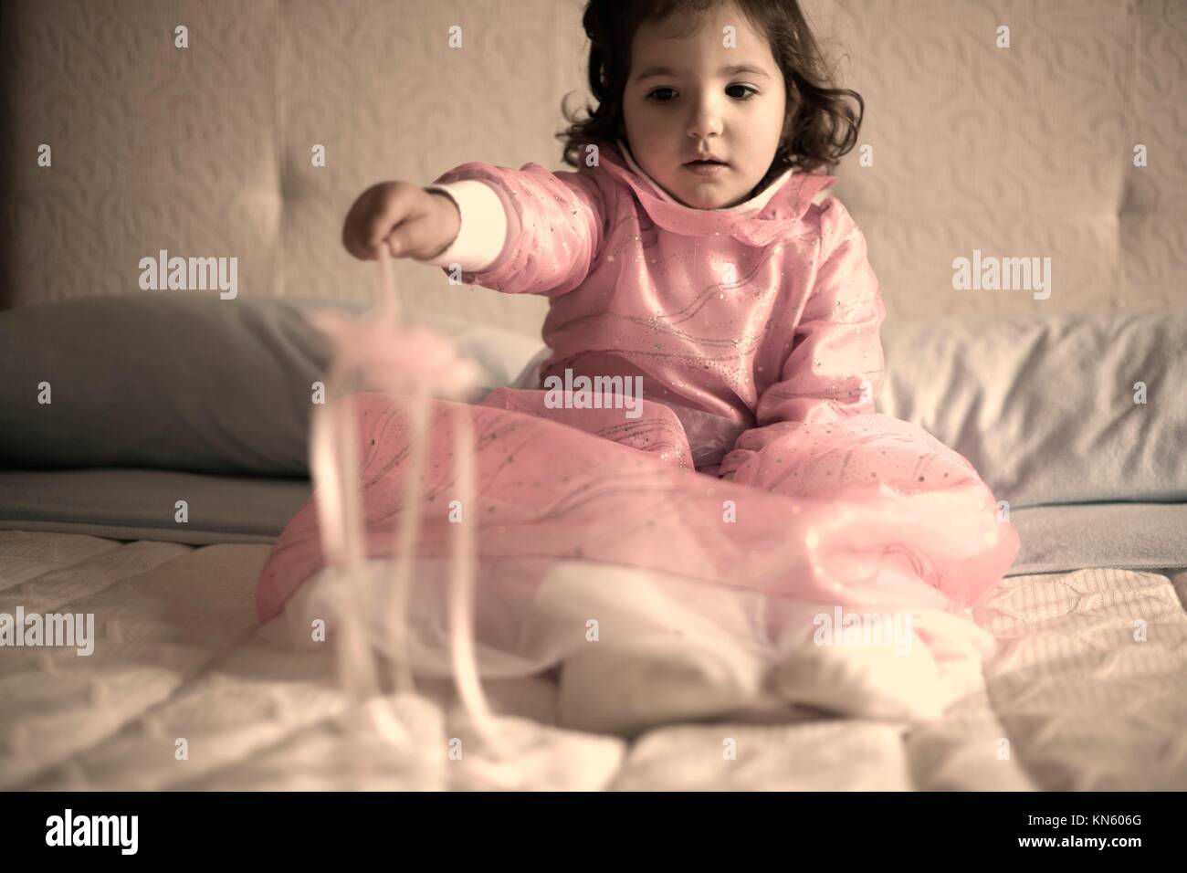 Little girl costumed as a fairy with magic wand sitting on the bed and playing. Stock Photo