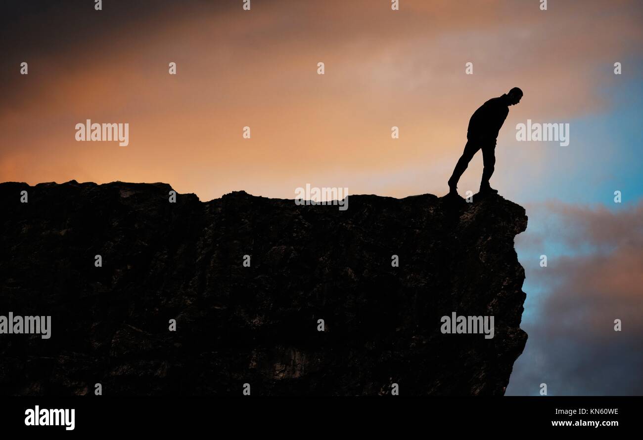 Distant view showing silhouette of hiking man standing on top of mountain looking down. Adventure in nature, a conceptual image of freedom and Stock Photo