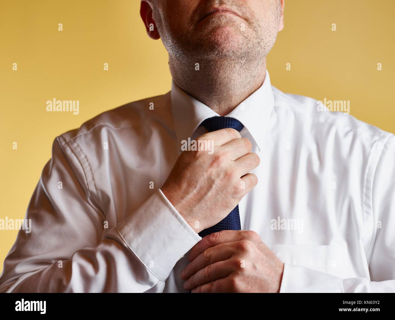 Close up, male wearing white shirt and blue tie, he tighten the tie knot, yellow background. Stock Photo