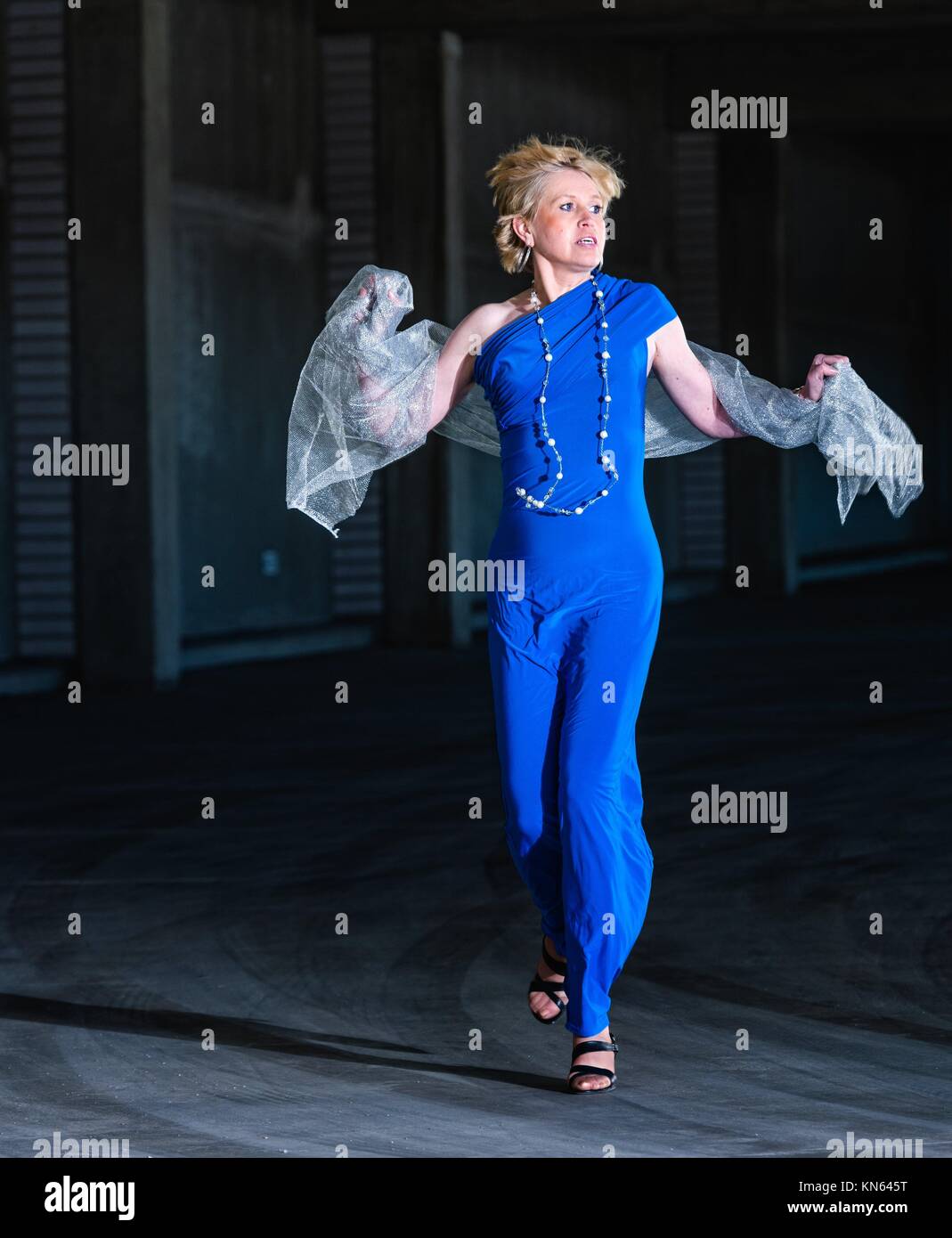 Frightened woman wearing blue dress and running in the public parking house. Stock Photo