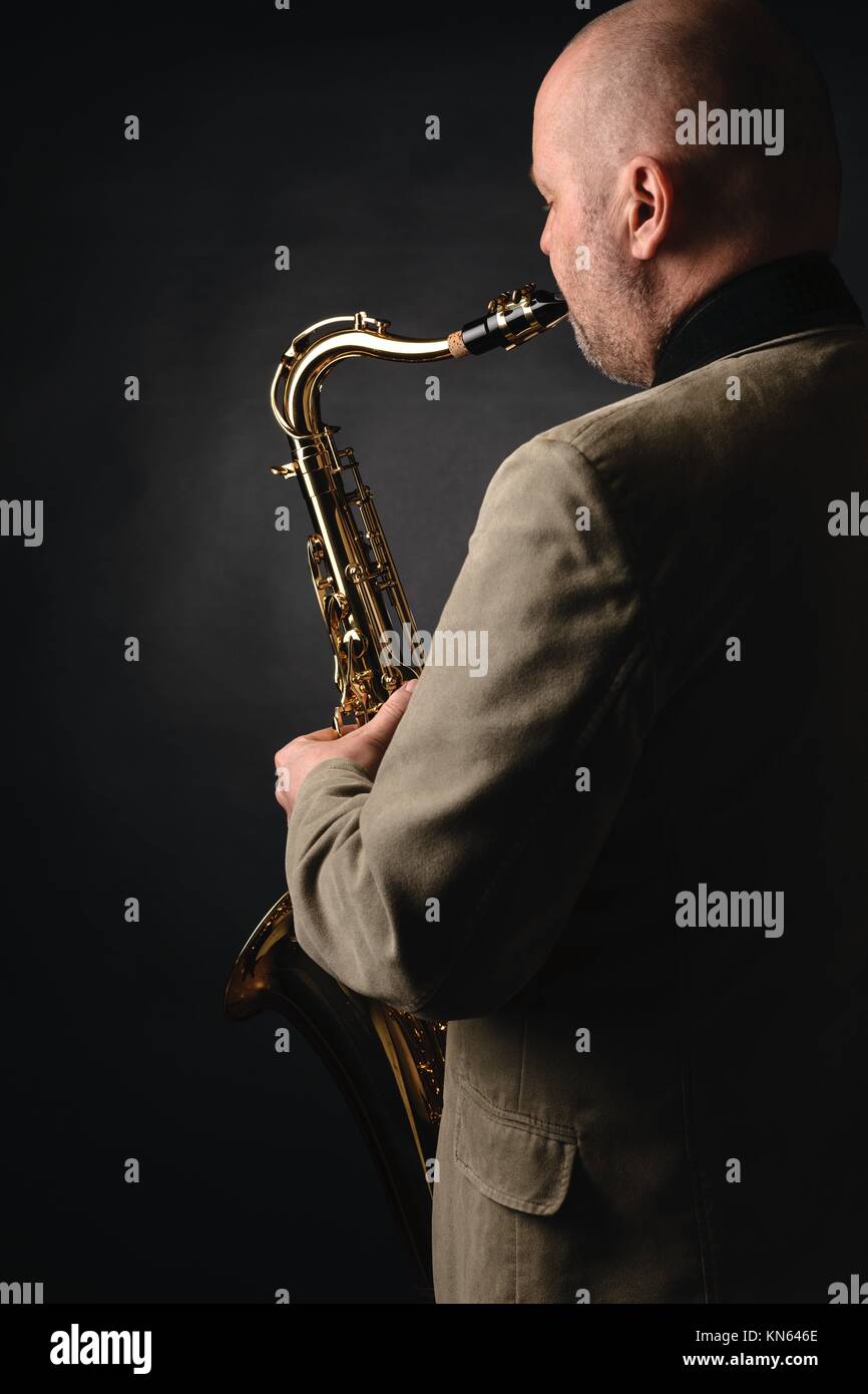 Adult musician playing tenor saxophone, over the shoulder view, dark background. Stock Photo