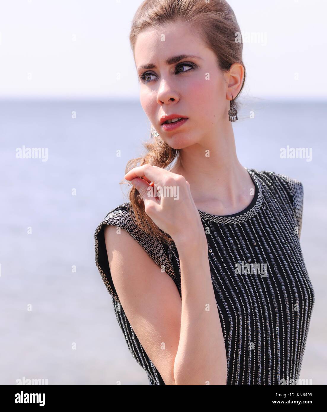 Fashionable woman on shore, she is wearing black dress with a stripes. Stock Photo