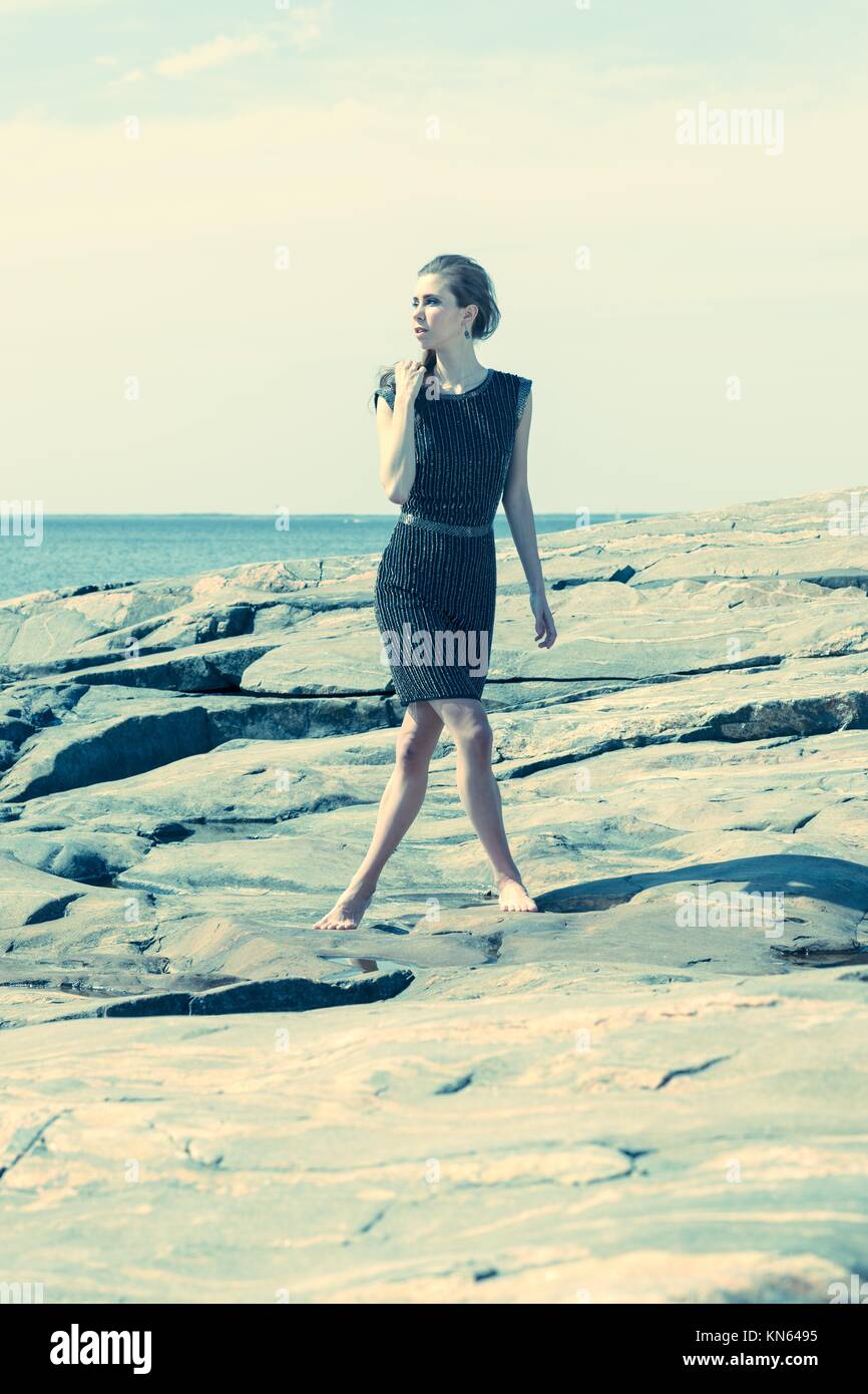Fashionable woman walking on the rocky shore, the horizon on background. Stock Photo