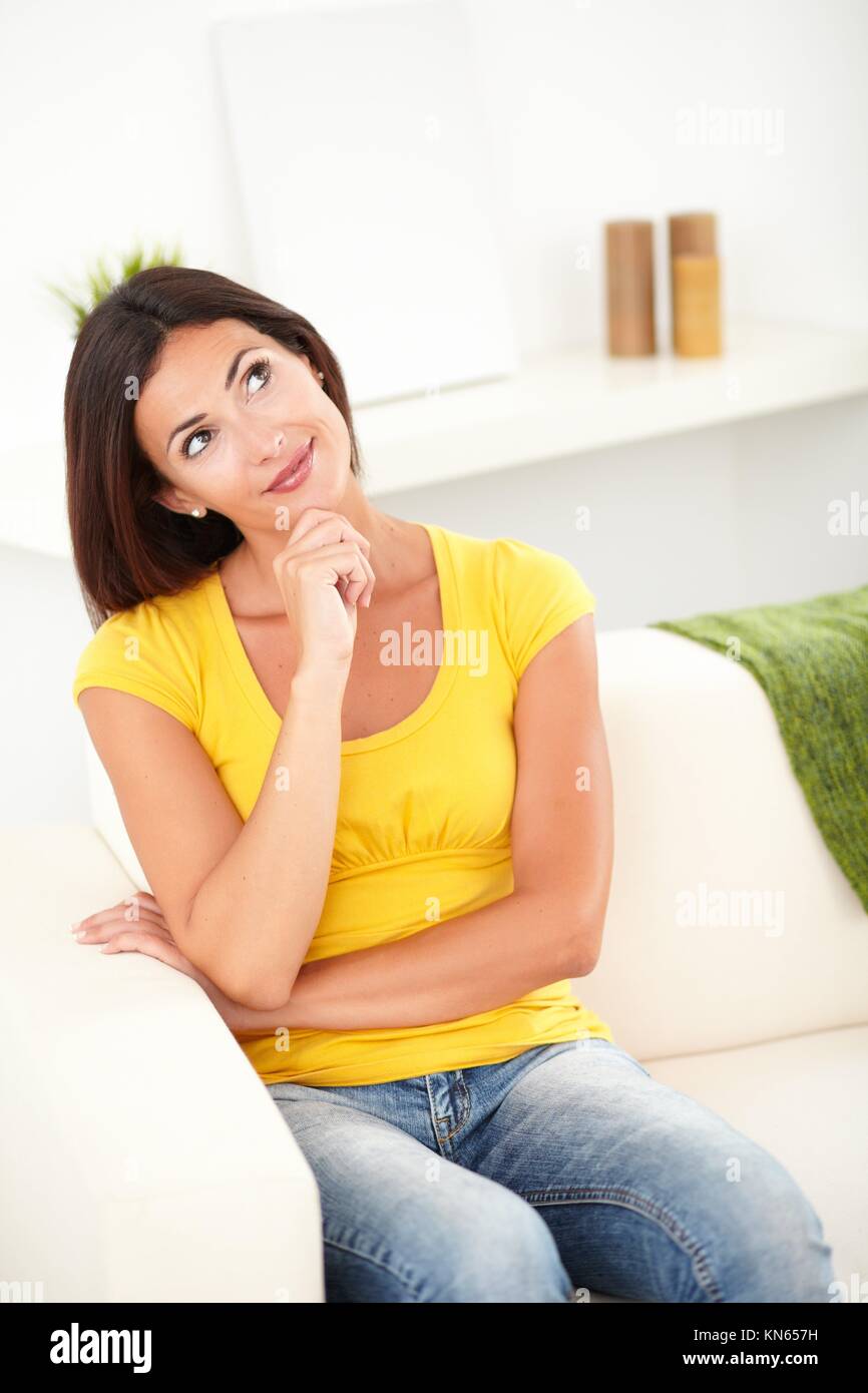 Three quarter length portrait of a beautiful woman thinking while sitting indoors. Stock Photo