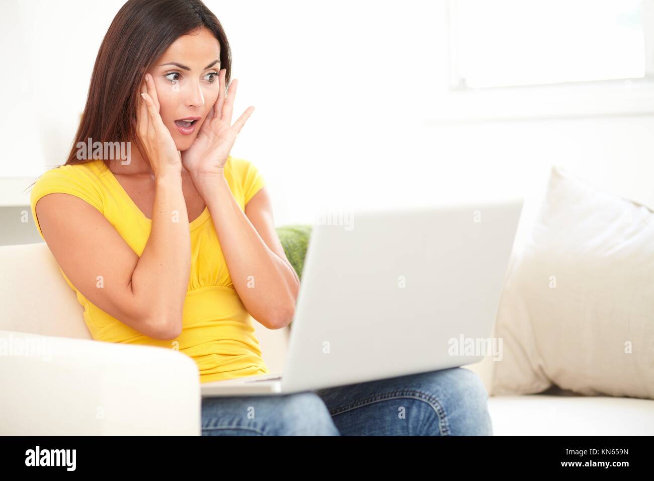 Young student with brown hair looking shocked while using a laptop indoors. Stock Photo