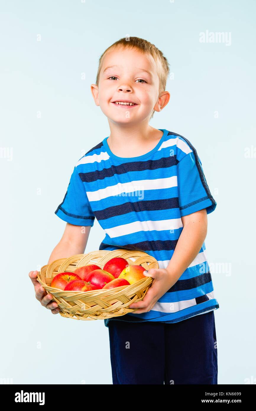 Little boy on striped t-shirt, fruit basket, studio shot and light blue ...