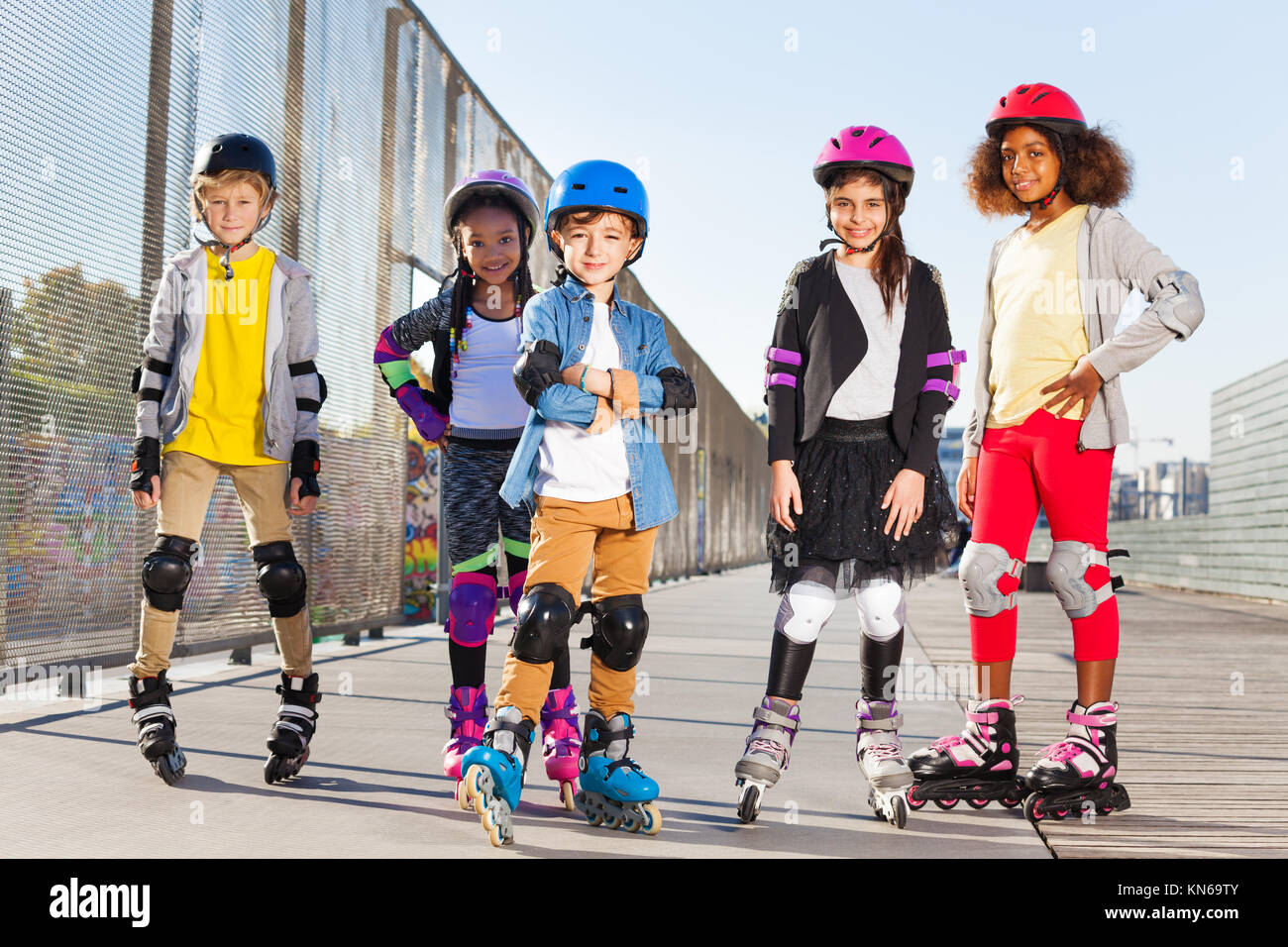 Happy schoolboy in roller helmet rollerblading with friends at stadium