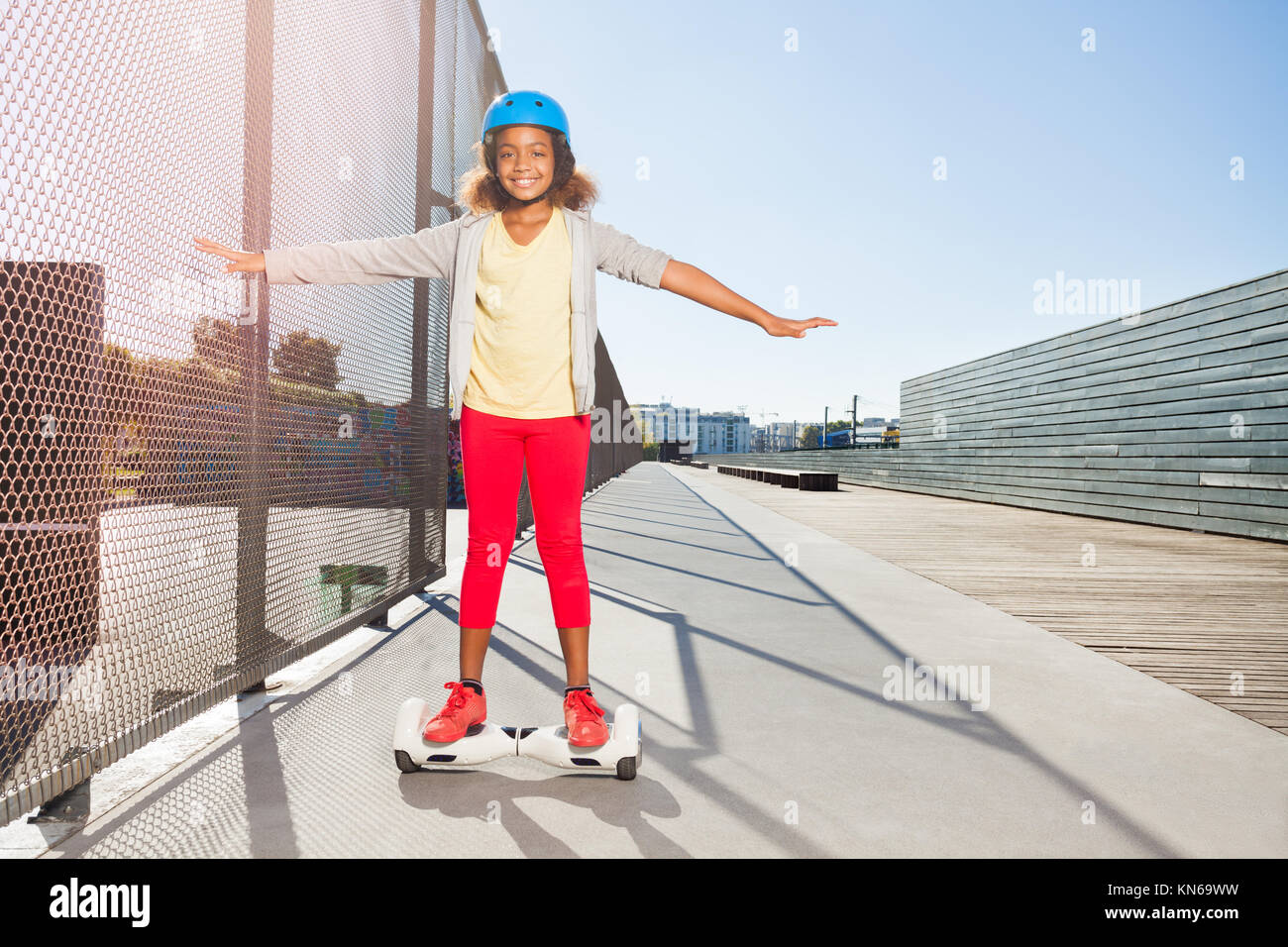African girl in helmet riding hoverboard or electric self balancing gyro scooter board on the side walk Stock Photo