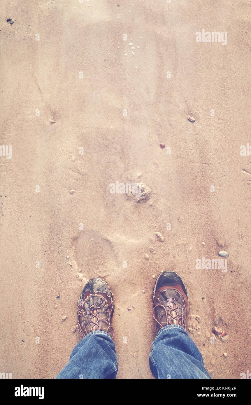 Person in hiking shoes stands on a beach, seen from above, color toned picture. Stock Photo