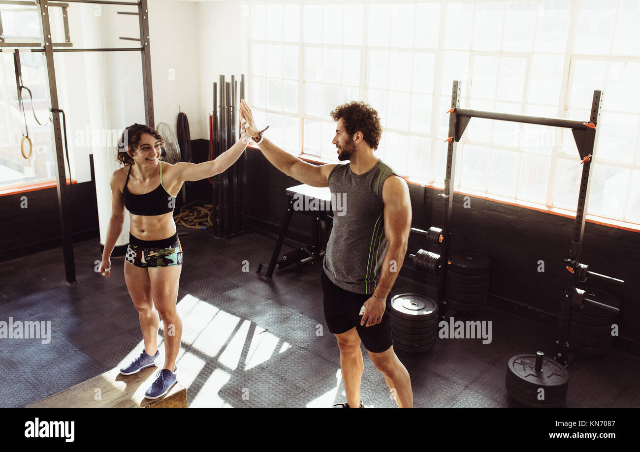 Man and woman standing on box and giving high five at gym. Male and female athletes doing box jump workout at cross training gym Stock Photo