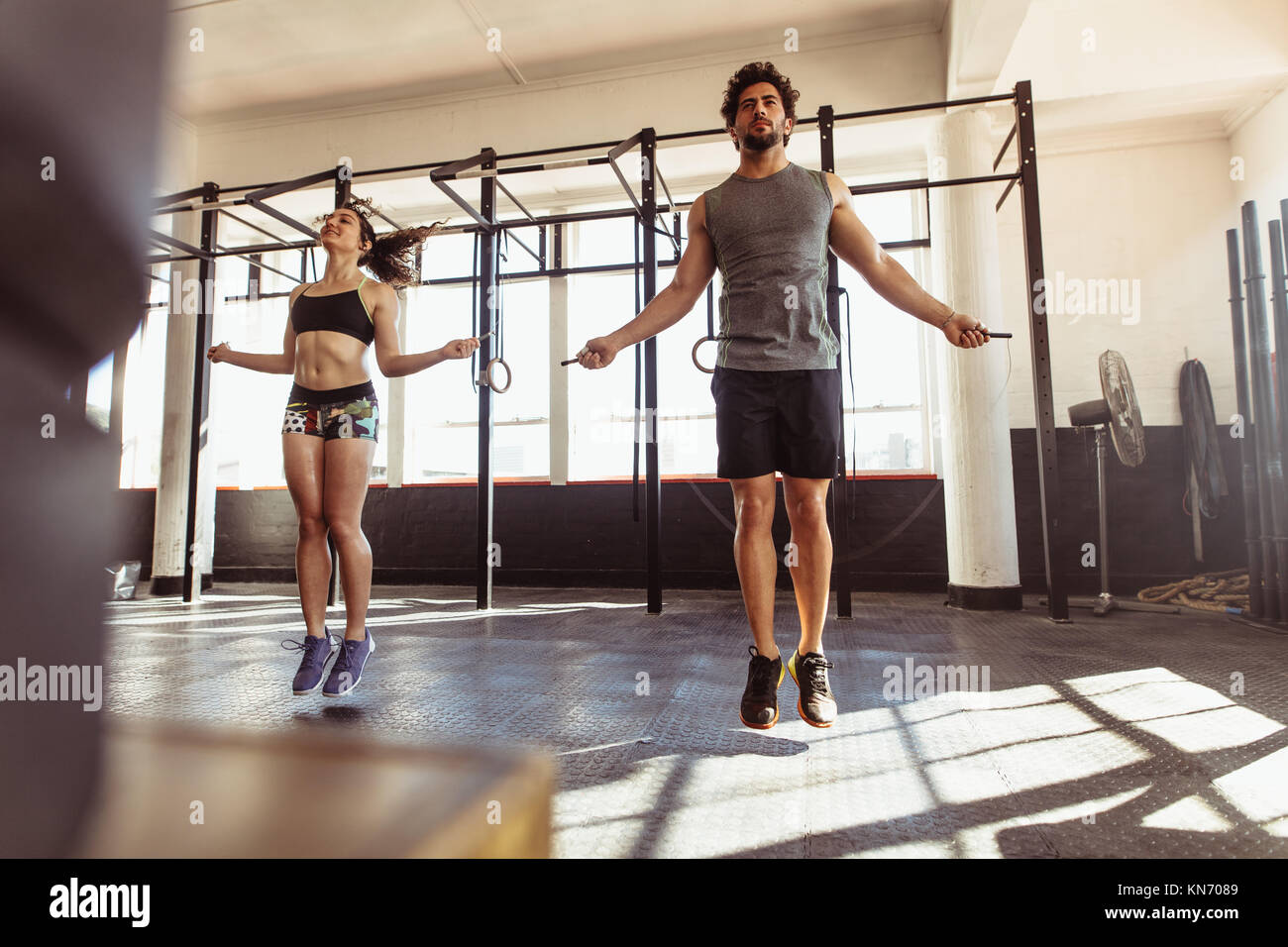 Muscular man and woman exercising using skipping rope in gym. Couple workout with jumping ropes in cross training gym. Stock Photo