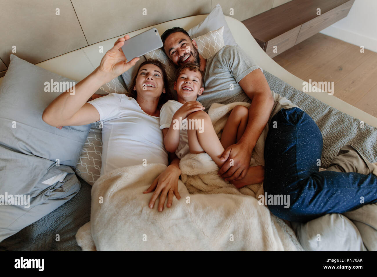 Family lying on bed and taking selfie at home. Happy young woman taking selfie with her family. Stock Photo