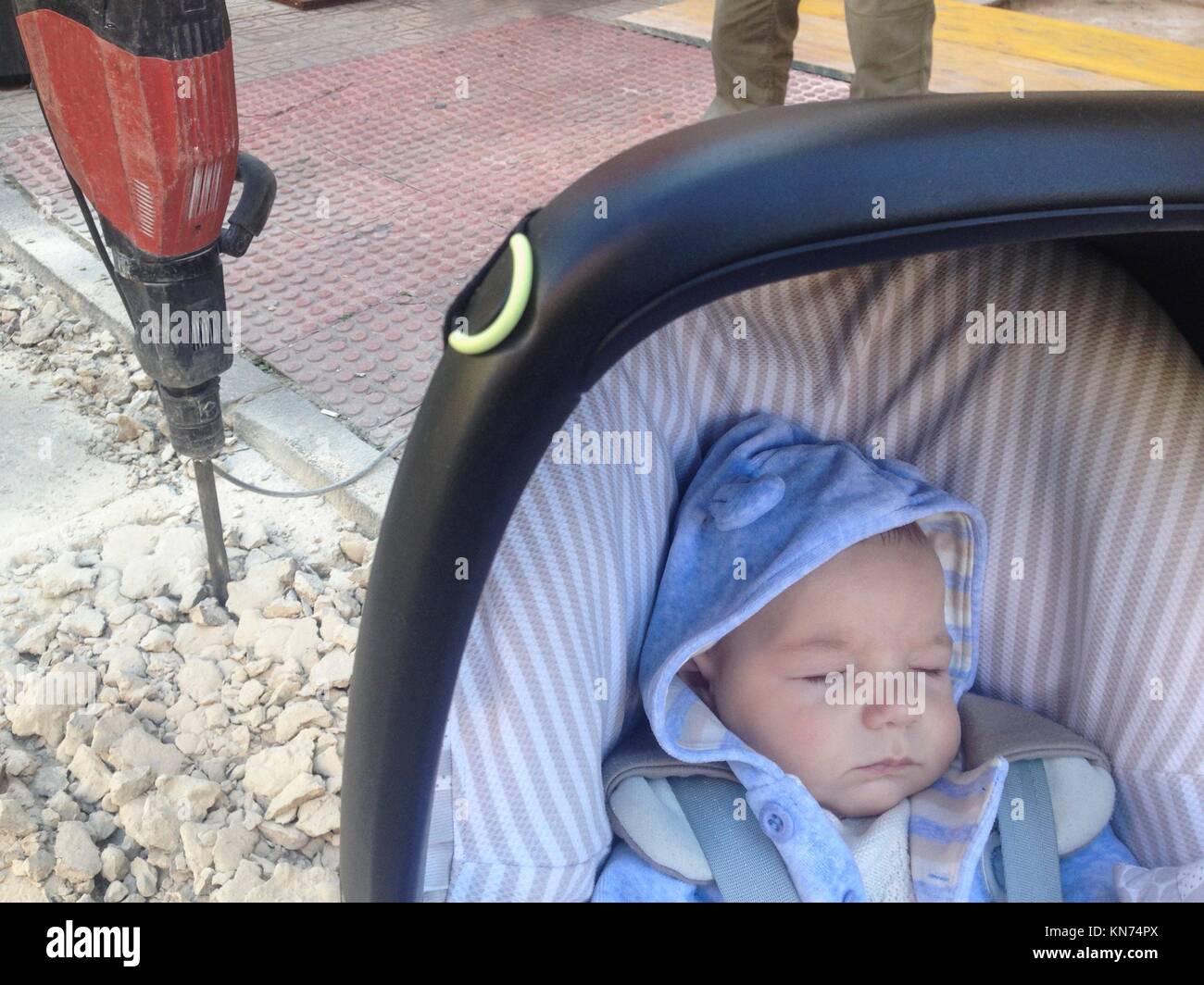 Sleeping four month baby boy lying in strolller getting close dangerously to jackhammer on the street. Stock Photo