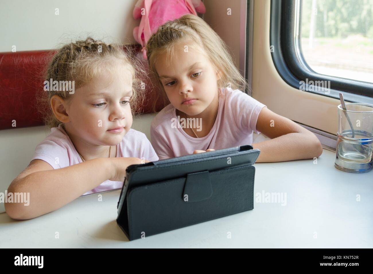 Two girls sisters sitting in the train watching a cartoon in the plate ...