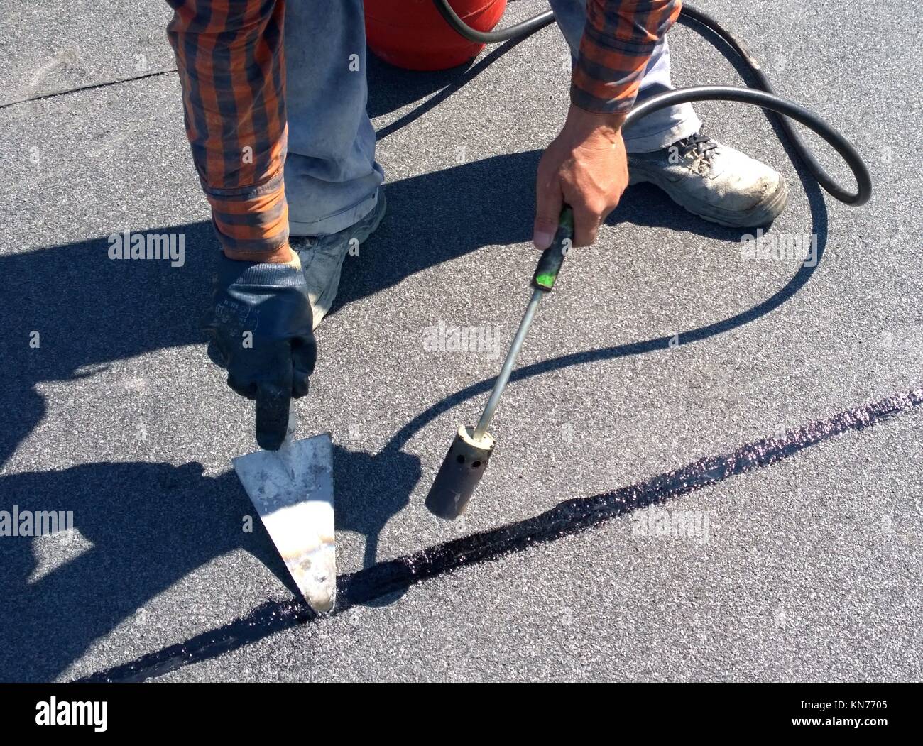 Roofer preparing part of bitumen roofing felt roll for melting by gas