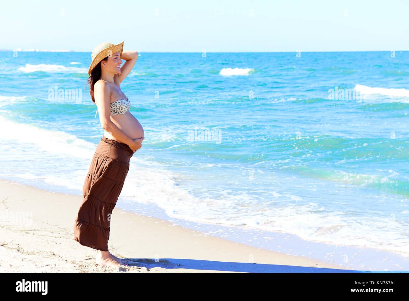 Beautiful pregnant woman on the beach with hat. Stock Photo