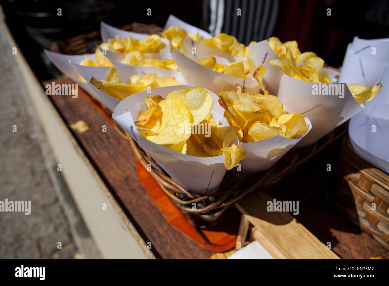 Fried potato chips in paper cornets for sell at market stall on wicker basket. Stock Photo