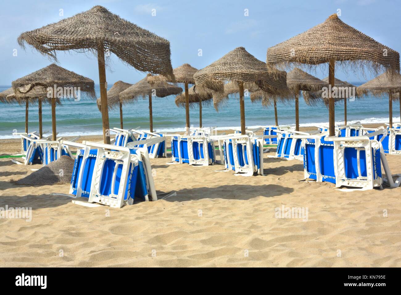 Rustic umbrellas made of natural fibers and sunbeds at Costa del Sol, Spain. Stock Photo