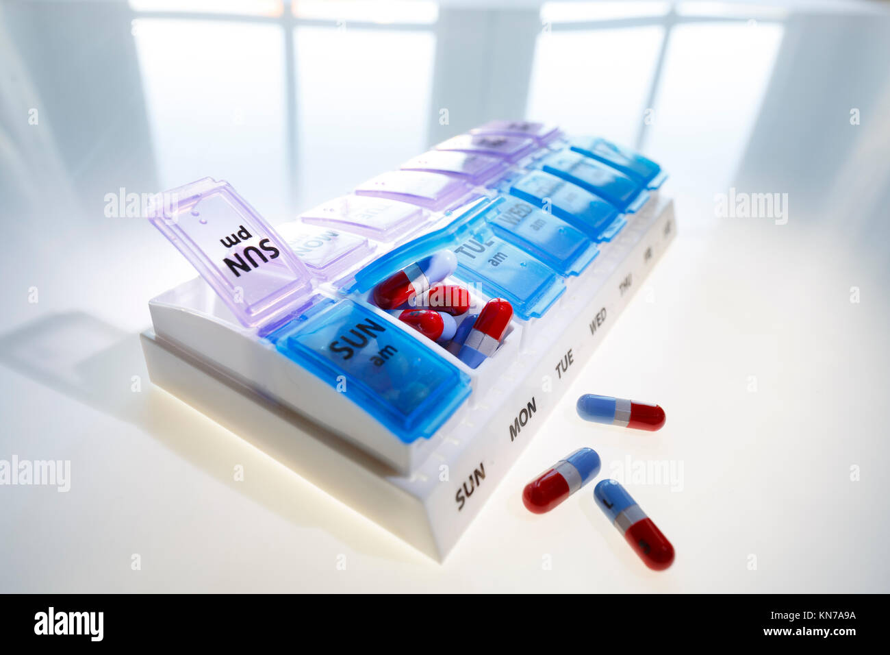 A weekly pill dispenser with one compartment open and full of tablets suggesting over medication Stock Photo