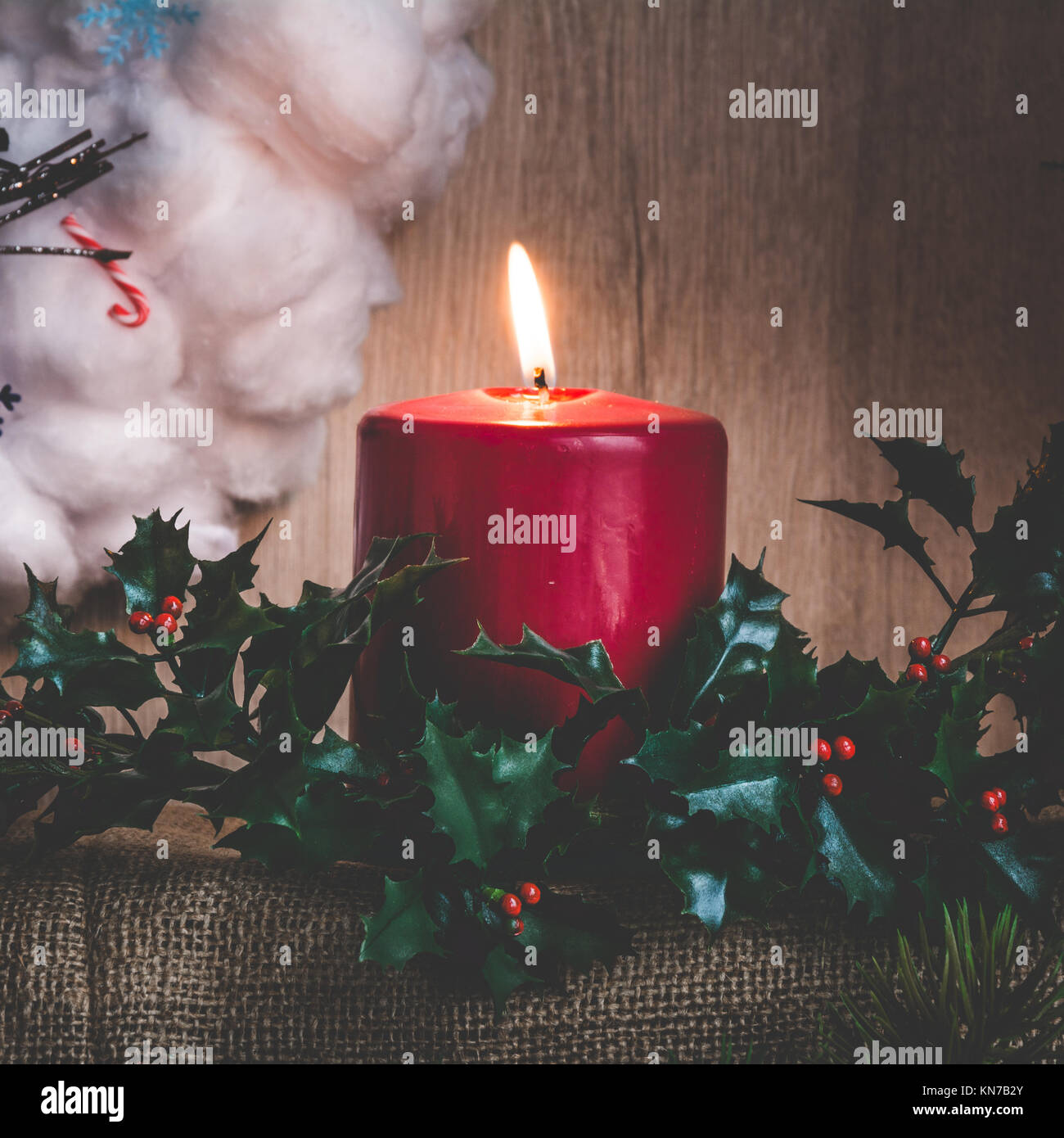 A burning candle and holly branches against the background of a ...
