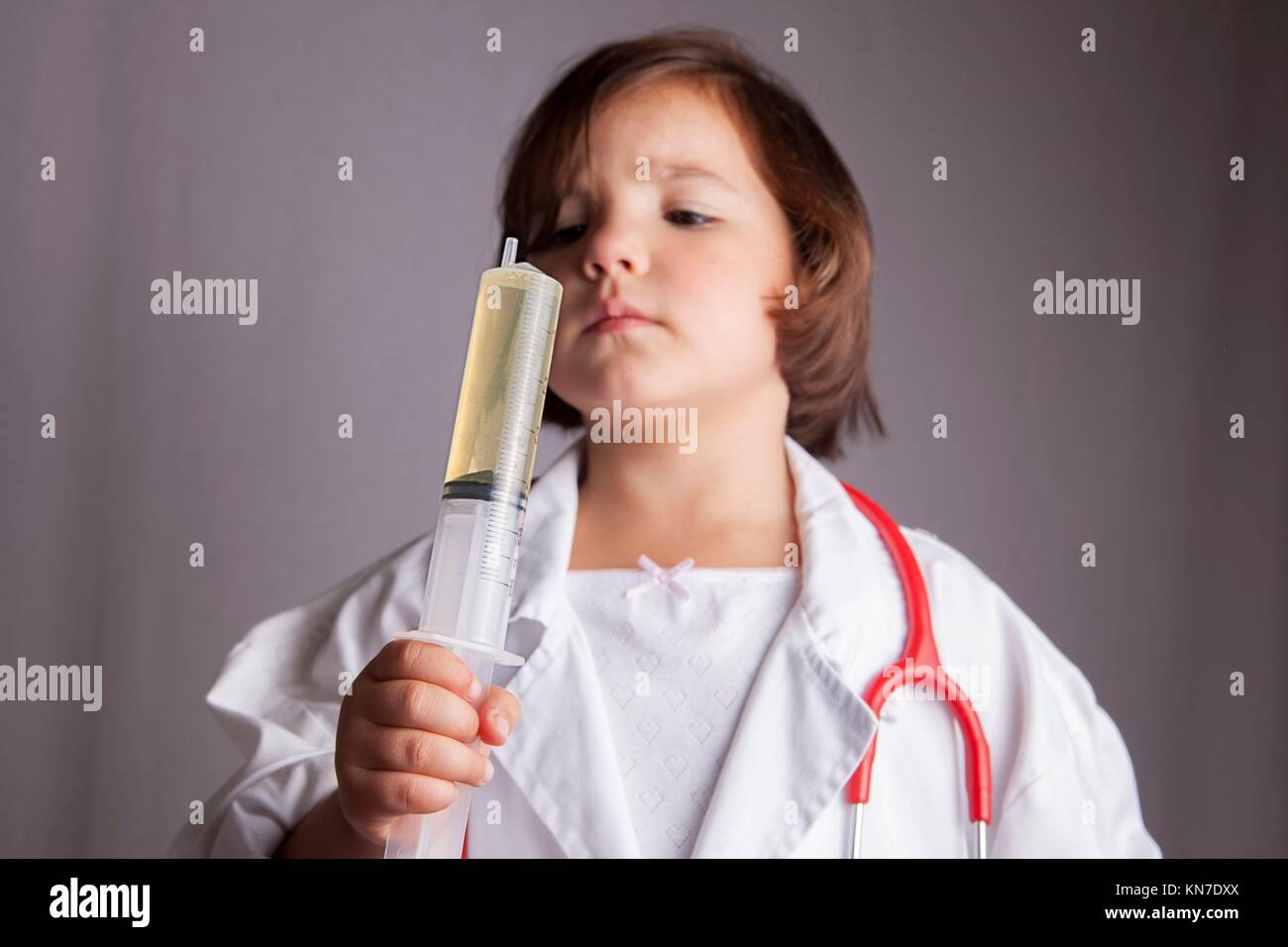 Little girl dressed as a doctor holding a huge syringe. Isolated over white background. Stock Photo
