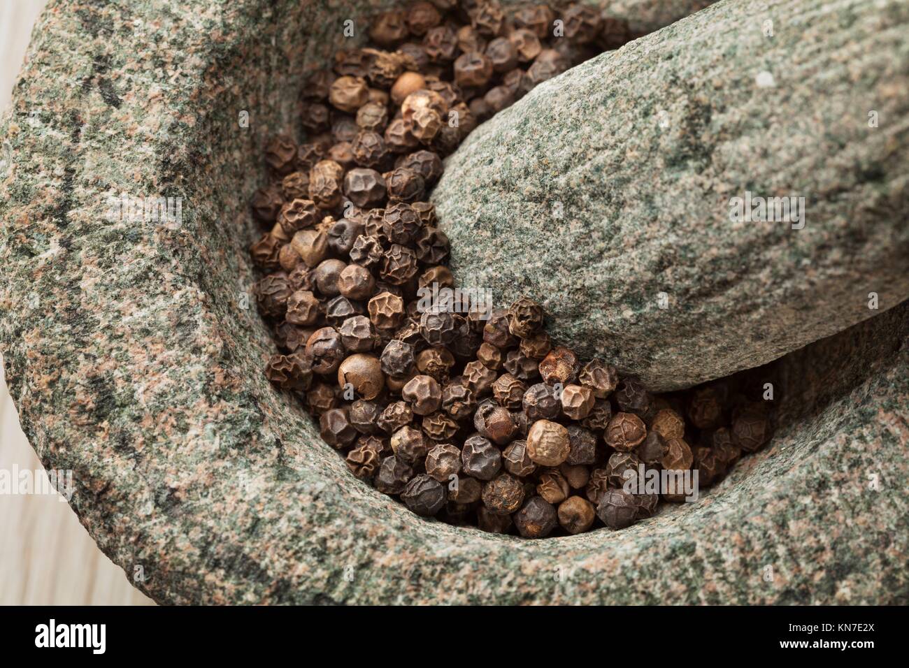 Traditional mortar and pestle with dried black pepper close up Stock