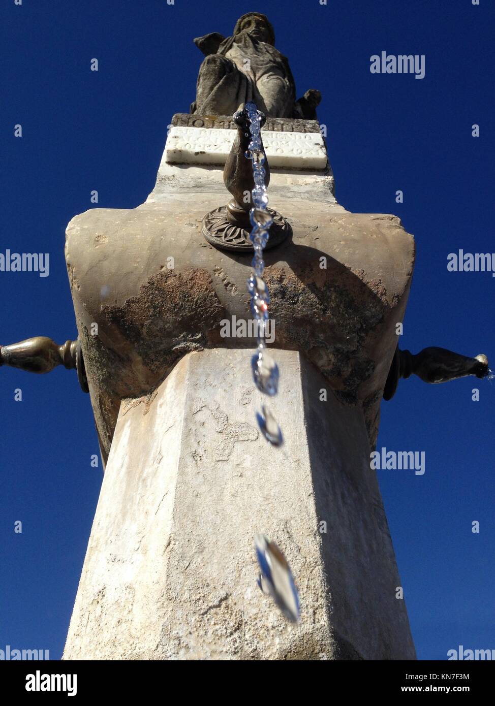 Close-up of an old stone fountain with dripping water and blue sky background. Low angle. Stock Photo