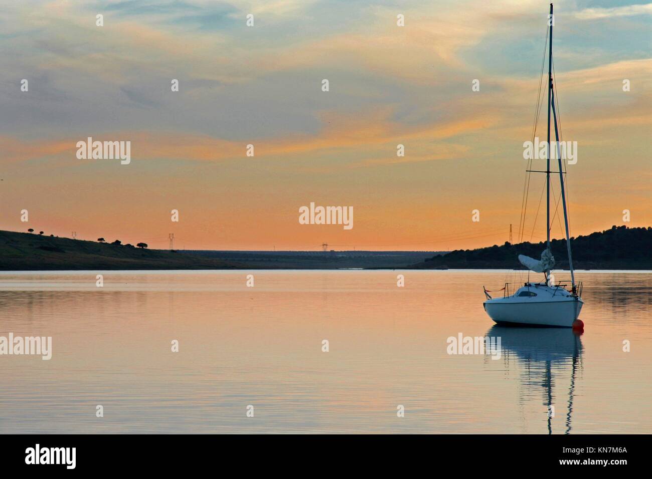 Sailboat anchored in the middle of Alange Reservoir, Spain. Sunset hour. Stock Photo