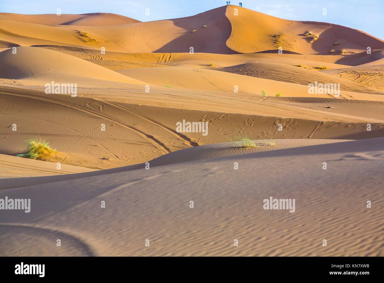 People admire the sunrise from a hill. Several sand hill at Erg Chebbi in the Sahara desert. Ers are large dunes formed by wind-blown sand. Stock Photo
